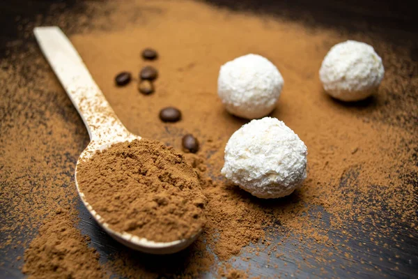 Three white truffles, a wooden spoon with cocoa, coffee grains on a black background