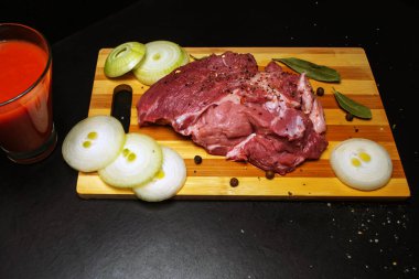 Kesme tahtasında taze et, bir bardak domates suyu.