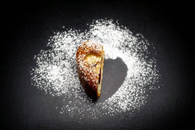 Kalp şeklinde pandispanya, üzerine pudra şekeri serpiştirilmiş. Siyah arkaplan.