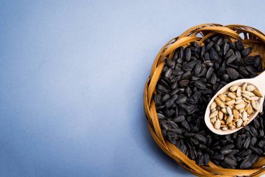 Hasır bir tabakta ay çekirdeği, gri bir zeminde tahta kaşıkta çekirdekler.