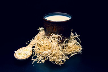 Siyah arka planda, tahta parçacıklarda, kilden bir bardaktaki süt.