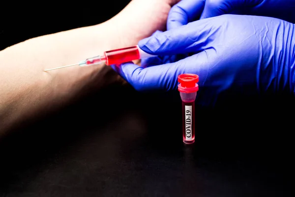 The doctor takes blood from a vein into a syringe, a test tube with coronavirus on a black background