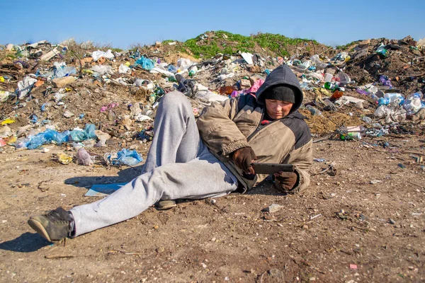Грязная Бездомная Лежит Земле Возле Свалки Смотрит Планшет — стоковое фото