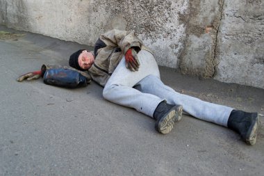 Evsiz, pis kadın duvarın altında yatıyor ve yerde uyuyor. Kadın çantası yakınlarda.