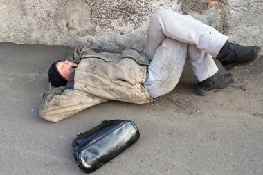 Evsiz, pis kadın duvarın altında yatıyor ve yerde uyuyor. Kadın çantası yakınlarda.