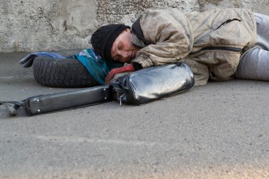 Evsiz, pis kadın duvarın altında yatıyor ve yerde uyuyor. Kadın çantası yakınlarda.