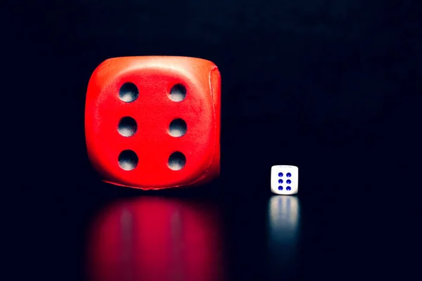 Big red dice next to a small white dice on a black background