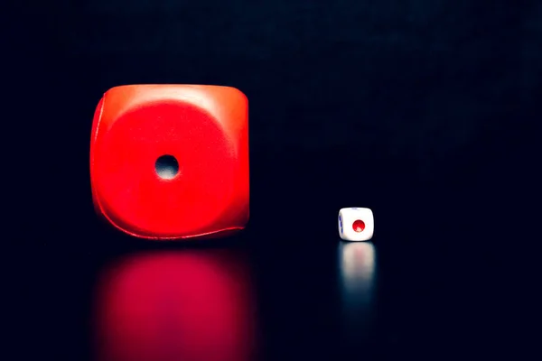 Big red dice next to a small white dice on a black background