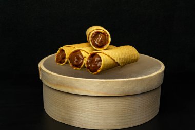 Wafer rolls with condensed milk on a wooden sieve on a black background clipart