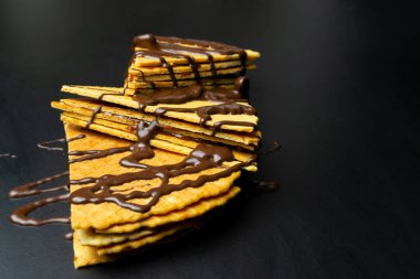 Yoğunlaştırılmış sütle waffle ruloları, siyah arka planda çikolatayla sulandırılmış.