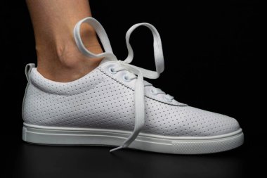 Beyaz spor ayakkabılar siyah arka planda bacakları üzerine giyilir. Spor ayakkabılar.