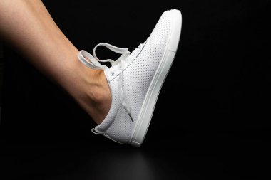 Beyaz spor ayakkabılar siyah arka planda bacakları üzerine giyilir. Spor ayakkabılar.