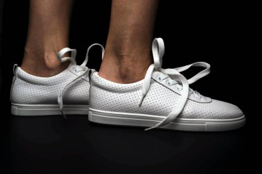 Beyaz spor ayakkabılar siyah arka planda bacakları üzerine giyilir. Spor ayakkabılar.