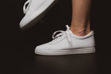 Beyaz spor ayakkabılar siyah arka planda bacakları üzerine giyilir. Spor ayakkabılar.