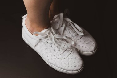 Beyaz spor ayakkabılar siyah arka planda bacakları üzerine giyilir. Spor ayakkabılar.