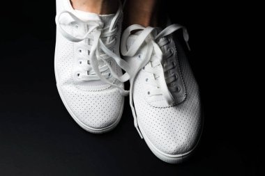 Beyaz spor ayakkabılar siyah arka planda bacakları üzerine giyilir. Spor ayakkabılar.