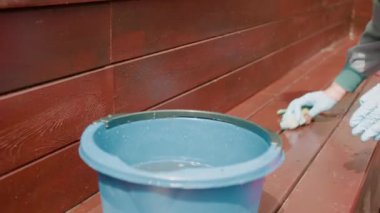 person cleaning brown wood close up partial view of human hands in gloves holding rag with bucket of water and cleaning brown wooden benches