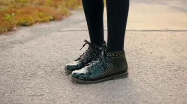 female legs in patent leather shoes standing on asphalt road close up teenager girl feet in black patent leather boots on path