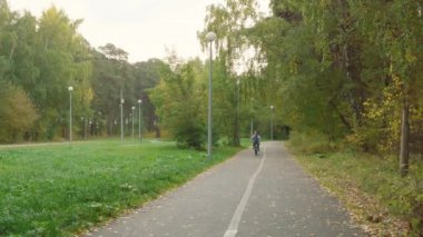 Çocuk parkta bisiklet sürüyor. Sevimli genç çocuk bisiklete biniyor ve güzel bir sonbahar parkında duygularını ifade ediyor.