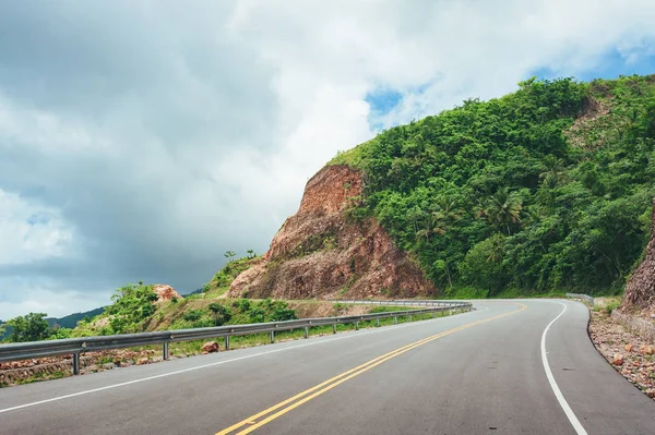 road crossing forest and hills with cloudy sky on background