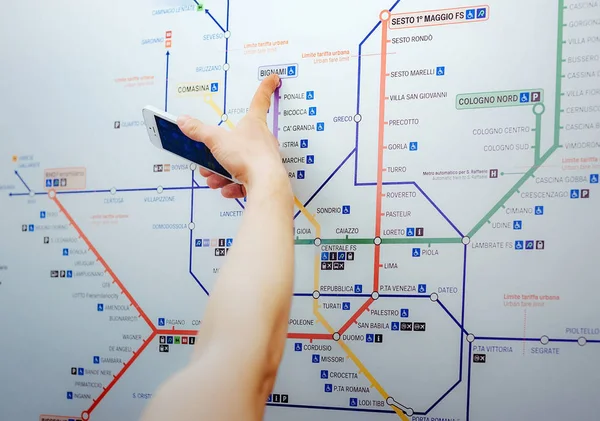 A tourist pointing the tourist attraction on a map public. The mans hand holds the phone and points to the map of the Italian subway trains
