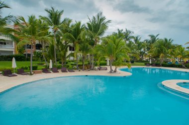 Havuz kenarındaki tropik bölgelerde tatil. Güneşin ışınları palmiye yapraklarının arasından parlıyor.