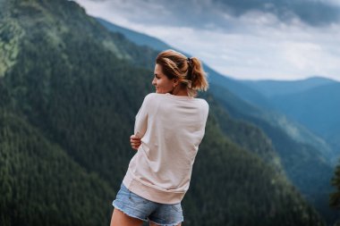 Genç bir kadın uçurumun kenarında duruyor ve gökyüzüne bakıyor..