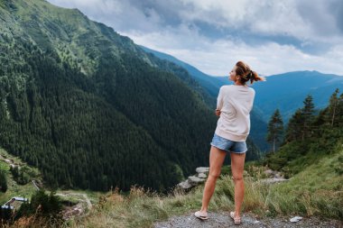 Genç bir kadın uçurumun kenarında duruyor ve gökyüzüne bakıyor..