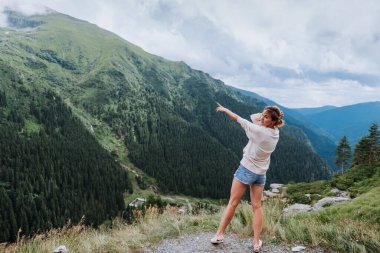 Genç bir kadın uçurumun kenarında duruyor ve elleri havada gökyüzüne bakıyor.