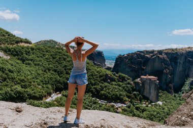 Bir kız Meteora 'nın, yani Yunanistan' ın uçurumunda duruyor ve vadiye bakıyor. yaz tatili