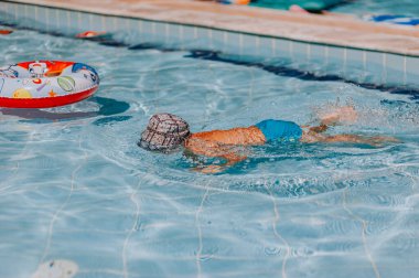 Mutlu genç çocuk yüzüyor ve suya dalıyor, çocuk havuzda eğlenerek kurbağalama vuruyor. Aktif sağlıklı yaşam tarzı, su sporları aktiviteleri ve çocuklarla yaz tatilinde ebeveynlerle dersler..