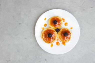 Böğürtlenli ve arka planda reçelli beyaz tabakta üç cheesecake.