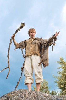 bir çuval bezi tişörtlü rustik adam ahşap bir personel kaldırma ve elini ileri uzanan bir taş üzerinde duruyor