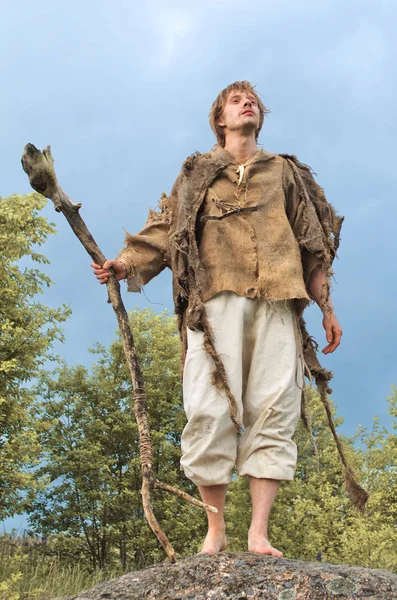 bir çuval bezi tişörtlü rustik adam tahta çubuğa yaslanmış bir taş üzerinde duruyor