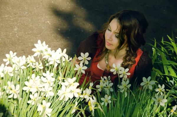 Ung kvinna satte sig för att vila nära en blomsterrabatt med påskliljor i — Stockfoto