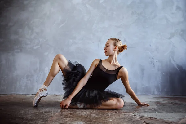 Young ballerina in a black dancing suit is posing in a loft studio — Stock Photo, Image