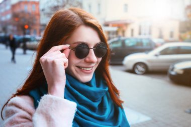 Kırmızı saçlı güzel şık kız şehirde bir ceket ve mavi eşarp sokak yürüyüş