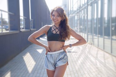 Uzun saçlı sportif kız şık bir gümüş şort renkli ve koyu yeşil t-shirt kentsel bir arka plan üzerinde egzersiz olduğunu... Fotoğraf durring bir güzel yaz sabah güneşin doğuşunu yapılır