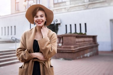 Kız kahverengi kabanlı bir kahverengi şapka yürüyüş ve şehir iç poz. Kız gülümsüyor, onun smartphone kontrol ve kahve içme kafe götürün.