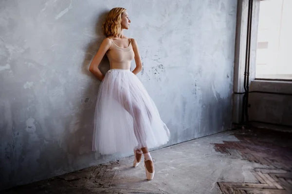 Young and slim ballet dancer is posing in a stylish studio with big windows — Stock Photo, Image