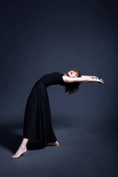 Dancer in a black dress is dancing in the dark studio