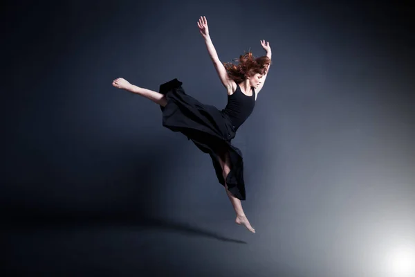 Dancer in a black dress is dancing in the dark studio — Stock Photo, Image