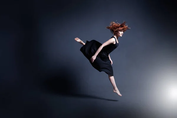 Танцовщица в черном платье танцует в темной студии — стоковое фото