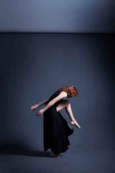 Танцовщица в черном платье танцует в темной студии — стоковое фото