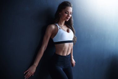Kadın fitness modeli beyaz üst ve siyah tayt içinde bir koyu mavi duvarın önünde poz