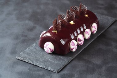 Kakao ayna sır macarons ve koyu gri arka plan üzerinde çikolata elemanları ile dekore edilmiş, çağdaş Siyah frenk üzümü çikolata Yule Log kaplı.