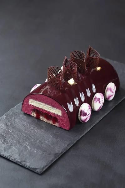 Kakao ayna sır macarons ve koyu gri arka plan üzerinde çikolata elemanları ile dekore edilmiş, çağdaş Siyah frenk üzümü çikolata Yule Log kaplı.