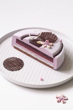 Çağdaş Blueberry Violet Mousse Kek kadife sprey ile kaplı ve beyaz zemin üzerine çikolata elemanları ile dekore edilmiş.