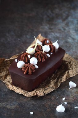 Çikolatalı Loaf Pastası çikolata jöleli, kremalı kurabiyelerle süslenmiş ve çikolatalı kremayla kaplanmış, kabartma kağıdıyla servis edilmiş, koyu arka planda.
