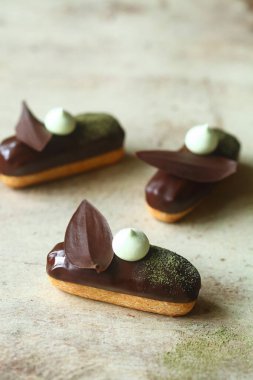 Geleneksel Fransız ekler Matcha Çay Pasta Kremi ile doldurulmuş ve çikolata jöleli, çikolata yapraklı ve kremalı kurabiyelerle süslenmiş, açık arkaplanda..